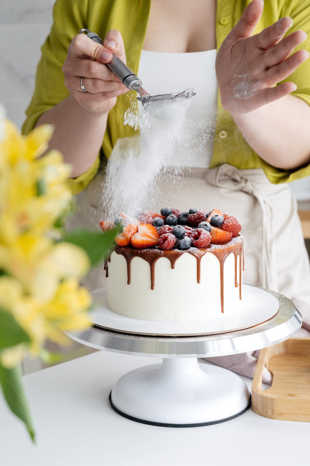 Woman Sprinkling Icing Sugar on Cake with Berries